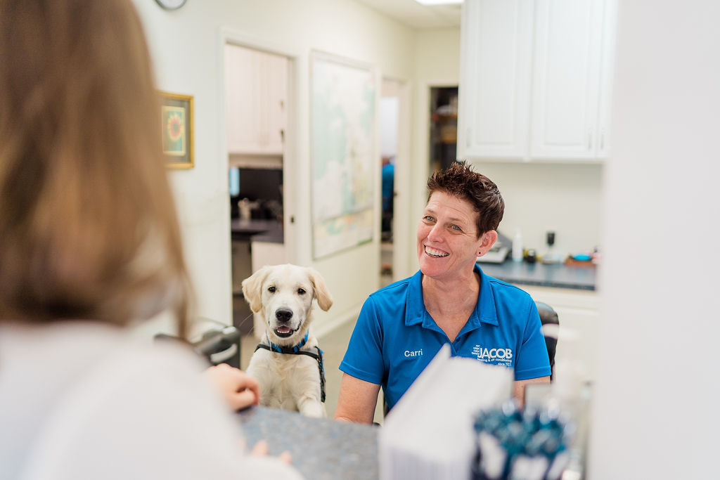 Jacob HAC emplyee sitting behind counter with a dog beside her, smiling at a customer