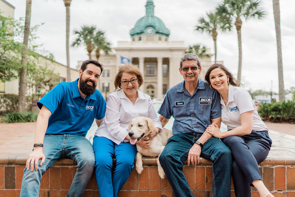 The Jacob family sits posing outside with their dog. 