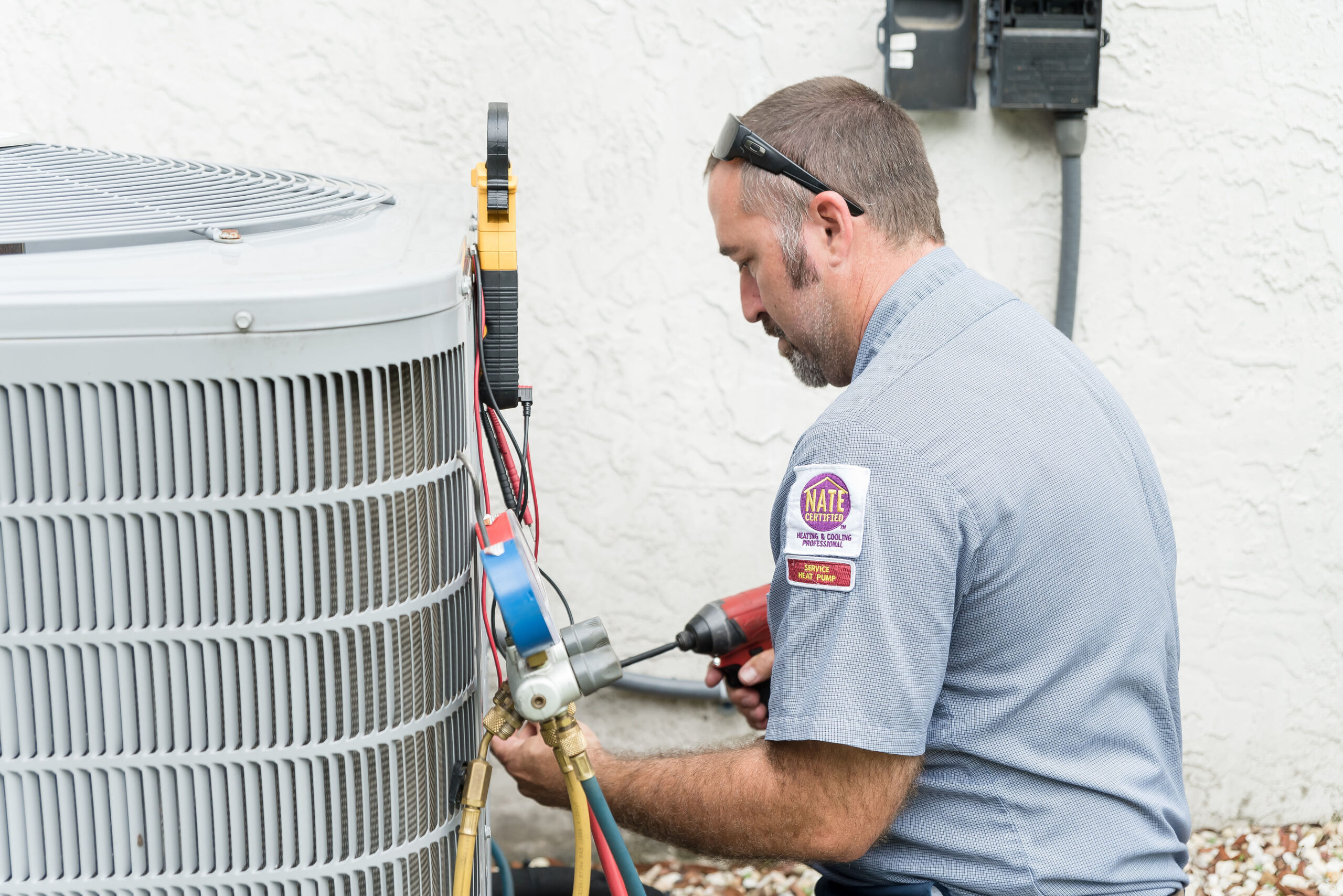AC technician repairing an outdoor AC unit next to a white stucco home.