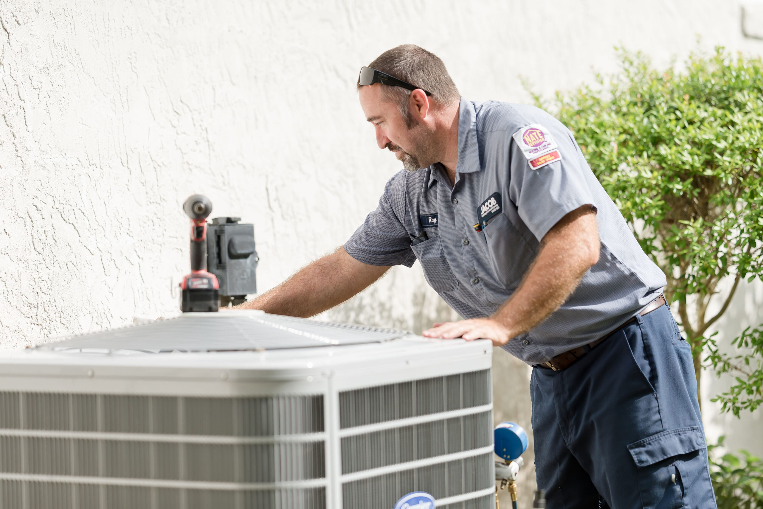 Technician working on an HVAC system outside a white stucco home.