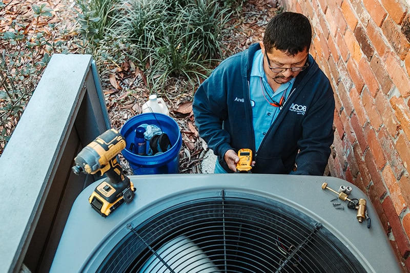 A man fixing an outdoor central air conditioning condenser unit (or heat pump) positioned in a backyard.
